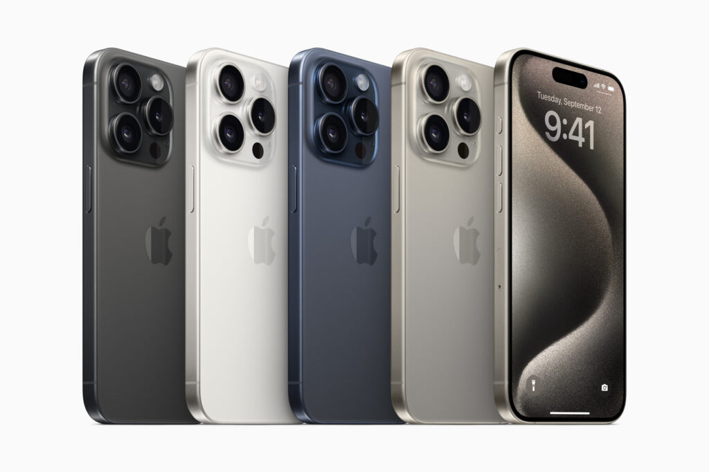 iPhone 15 Pro Max in titanium finish, showing the rear camera module and edge-to-edge display on a reflective surface.
