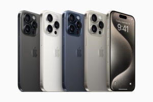 apple iPhone 15 Pro Max in titanium finish, showing the rear camera module and edge-to-edge display on a reflective surface.